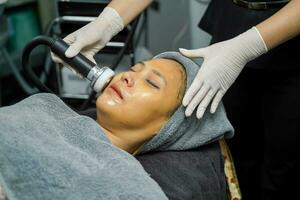de cerca asiático belleza mujer teniendo terapia a estimular facial piel y facial ultrasónico protección de la piel tratamiento por profesional cosmetóloga bienestar. foto