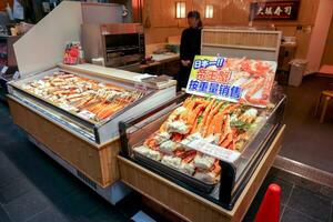 Osaka City, Japan, 2019 - Lot of burned king crab legs and prawn in a small seafood freezer display with Japanese colorful sign and price tags front of seafood shop in fresh market. photo