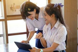 Happiness cheerful Thai girls student looking a social network on tablet in the coffee shop with bright sun flare background. photo