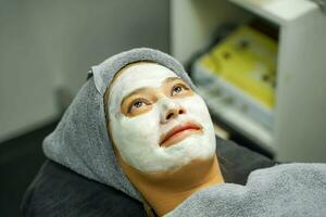 de cerca belleza mujer con blanco máscara crema en su cara en belleza clínica. foto