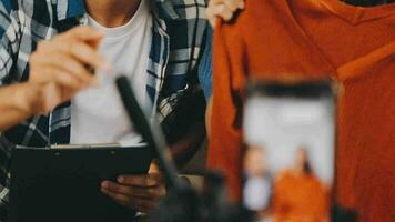 joven asiático mujer negocio propietario a Moda Tienda utilizando Teléfono móvil En Vivo transmisión para rebaja Moda sombrero y ropa. influencers grabar vídeo revisión articulo para vender en social medios de comunicación. en línea compras video