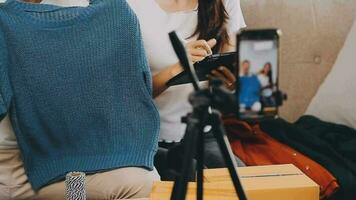 joven asiático mujer negocio propietario a Moda Tienda utilizando Teléfono móvil En Vivo transmisión para rebaja Moda sombrero y ropa. influencers grabar vídeo revisión articulo para vender en social medios de comunicación. en línea compras video