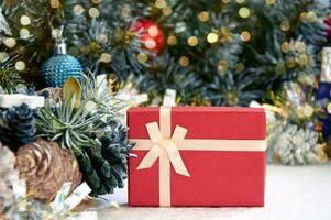 Christmas composition with fir tree branches, red gift box and silver tinsel in golden light of garland photo