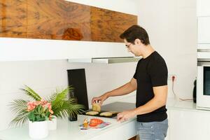 Adult man standing near cooking range and toasting bread slices in kitchen photo