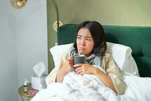 gripe, enfermedad y gente. joven mujer sensación enfermo, teniendo fiebre y atrapando columna, acostado en cama con caliente té, tomando drogas desde influenza foto