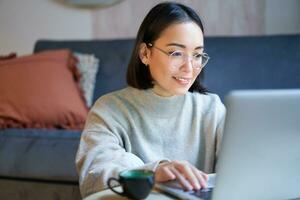 Portrait of smiling asian girl working from home, staying on remote, using laptop, studying on her computer photo