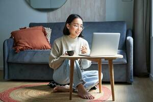 Portrait of beautiful young woman professional, working on remote from home, freelancing with her laptop, video chats, drinks coffee photo