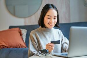 Portrait of korean woman shopping online, using her credit card and laptop to order delivery from website photo