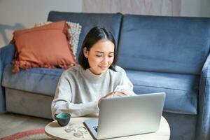 trabajo desde hogar, Lanza libre y e-learning concepto. joven mujer estudiando, sentado en frente de computadora portátil, trabajando en remoto, lugar de trabajo en vivo habitación foto