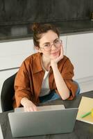 Vertical shot of woman working from home, business owner using laptop, browsing social media on computer, wearing glasses photo