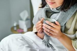 Close up of female hands holding hot drink, lying in bed, girl catching a cold and staying at home photo