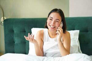 Woman talks on mobile phone in bed. Smiling girl having telephone conversation while relaxing in bedroom photo