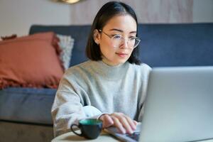 yo empleado joven coreano mujer trabajando en remoto, mecanografía en computadora portátil, estudiando a hogar en vivo habitación foto