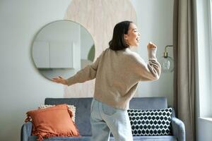 Beautiful asian woman dancing, feeling happy and upbeat, singing into hand microphone, express joy, positivity and happiness photo