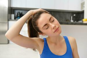 Portrait of woman workout from home, does training exercises, stretches her neck, warm-up before fitness photo