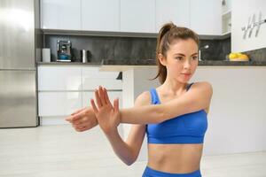 Image of fitness girl concentrates on workout, stretches hands before training session at home, follows online gym instructions photo