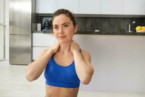 Close-up potrait of fitness woman, does training, workout from home, massaging neck, exercise in living room photo