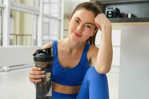 Beautiful young sportswoman drinks water, stays hydrated during workout training at home, doing fitness exercises in living room photo