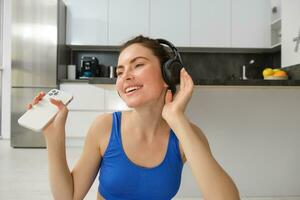 felicidad, Deportes y bienestar. joven mujer bailando en auriculares, participación teléfono inteligente, haciendo rutina de ejercicio a hogar, aptitud formación dentro su casa foto