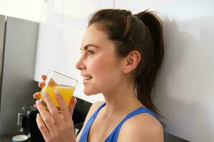Shot of sporty beautiful woman drinking detox juice in the kitchen at home photo