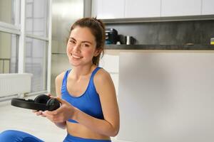 Portrait of woman doing home fitness exercises on yoga mat, listening music in wireless headphones, focusing on workout in earphones photo