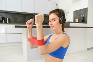 Young woman doing fitness workout at home, using elastic resistance band on arms, muscle exercises, sitting on rubber mat in living room photo