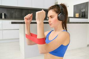 Portrait of determined beautiful woman, listening music, workout with elastic resistance band, doing exercises on arms, wearing sportsbra photo