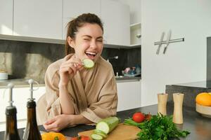 retrato de morena mujer, esposa Cocinando a hogar, haciendo cena, posando cerca el cortar tablero en cocina con verduras, participación calabacín foto