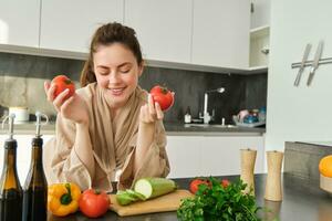 Portrait of beautiful woman cooking in the kitchen, chopping vegetables on board, holding tomatoes, lead healthy lifestyle with preparing fresh salads, vegan meals photo