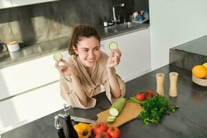 Portrait of beautiful brunette girl chopping vegetables for meal, making salad in the kitchen, eating healthy food, preparing dinner photo