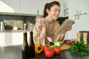 Portrait of modern young woman cooking, making grocery list, reading recipe and making meal, salad in the kitchen, looking at vegetables on chopping board photo