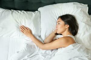 Portrait of romantic asian woman lying alone in her bed, touching empty pillow and thinking about her partner, breakup relatioship photo