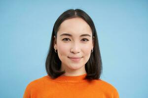 Close up of candid young asian woman, looking at camera with genuine, natural emotions, standing over blue background photo