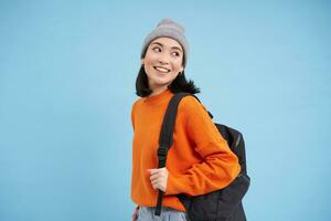 belleza y protección de la piel. cerca arriba retrato de contento sonriente japonés mujer, toques su claro, brillante piel, natural sano rostro, en pie terminado azul antecedentes foto