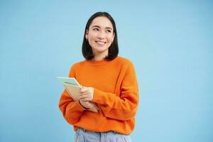 Beauty and skincare. Close up portrait of happy smiling japanese woman, touches her clear, glowing skin, natural healthy face, standing over blue background photo