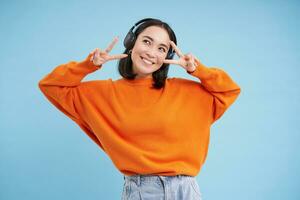 Beauty and skincare. Close up portrait of happy smiling japanese woman, touches her clear, glowing skin, natural healthy face, standing over blue background photo