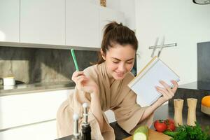Portrait of woman cooking in the kitchen, reading her notes, checking recipe while preparing meal, making breakfast salad, writing down grocery list photo