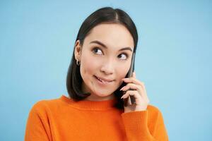 Beauty and skincare. Close up portrait of happy smiling japanese woman, touches her clear, glowing skin, natural healthy face, standing over blue background photo