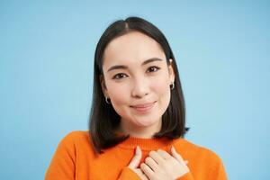 cerca arriba retrato de hermosa coreano mujer con sano sonrisa, natural claro facial piel, soportes terminado azul antecedentes foto