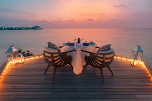 Amazing romantic dinner on the beach on wooden deck candles under sunset sky. Romance and love, luxury destination dinning, exotic table setup with sea view. Honeymoon proposal design photo