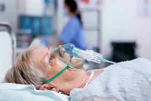 Old woman breathing with oxygen mask laying in hospital bed getting treatment for infection with coronavirus. Medicine medical healthcare system epidemic lungs infection treatment photo