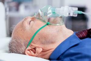 Sick old man with respiratory mask laying on hospital bed after being infected with coronavirus. Medicine medical healthcare system epidemic lungs infection treatment photo