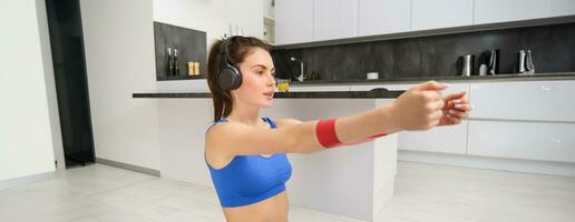 imagen de trabajo duro deportista, niña haciendo aptitud ejercicios a hogar, escuchando música en auriculares, extensión elástico resistencia banda con brazos, rutina de ejercicio en vivo habitación foto