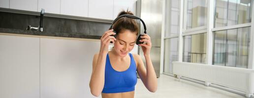 Young woman doing workout training at home, puts on her wireless headphones photo