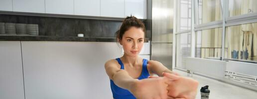 Close up portrait of active and healthy young woman, stretching her arms, workout from home, doing fitness exercises, aerobics training in living room, looking focused photo