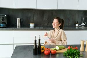 retrato de mujer pensando de menú, sentado en el cocina y haciendo tienda de comestibles lista, vegetales y comida ingredientes en mostrador foto