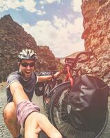 Male caucasian crazy cyclist by bicycle have funny expression outdoors pose on cycling trip. Travel around world cyclist experience documenting photo