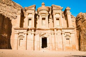 Cinematic Petra background caucasian young woman in white dress and hat enjoying Petra A'deir Monastery, Petra's largest monument, UNESCO World Heritage Site, Jordan. photo