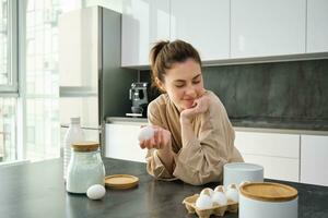 Attractive young cheerful girl baking at the kitchen, making dough, holding recipe book, having ideas photo