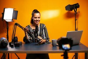 Influencer smiling into camera and recording podcast in studio. Social media star making online internet content about video equipment for web subscribers and distribution, film photo